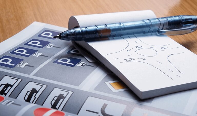 Driving school materials with parking signs, road diagrams, and a pen on a wooden desk.