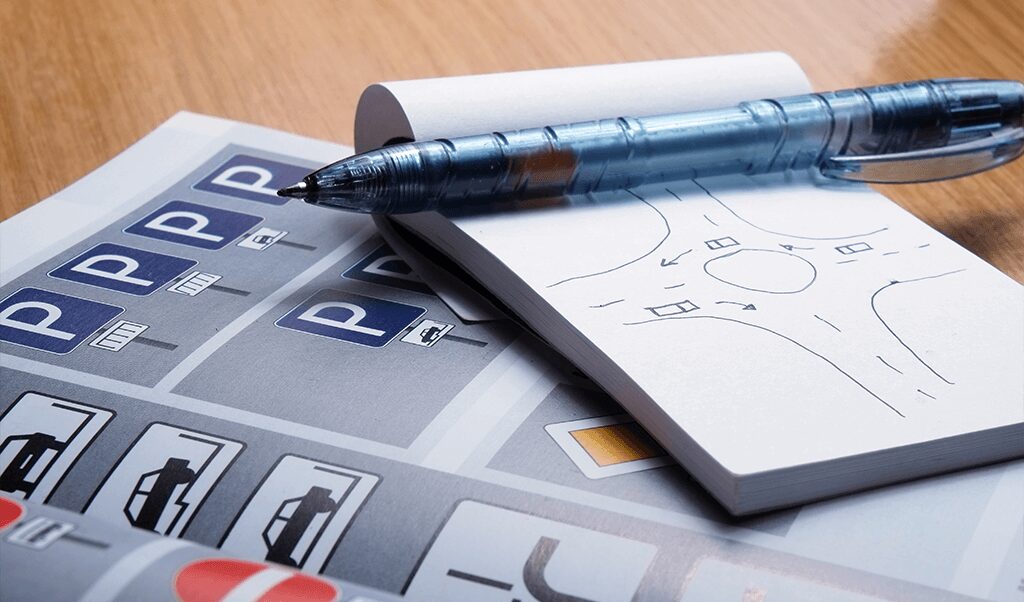 Driving school materials with parking signs, road diagrams, and a pen on a wooden desk.